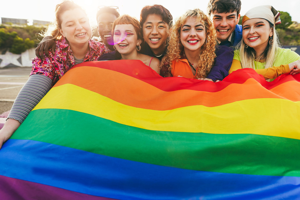 A group of LGBT youth holding a rainbow flag in front of themselves